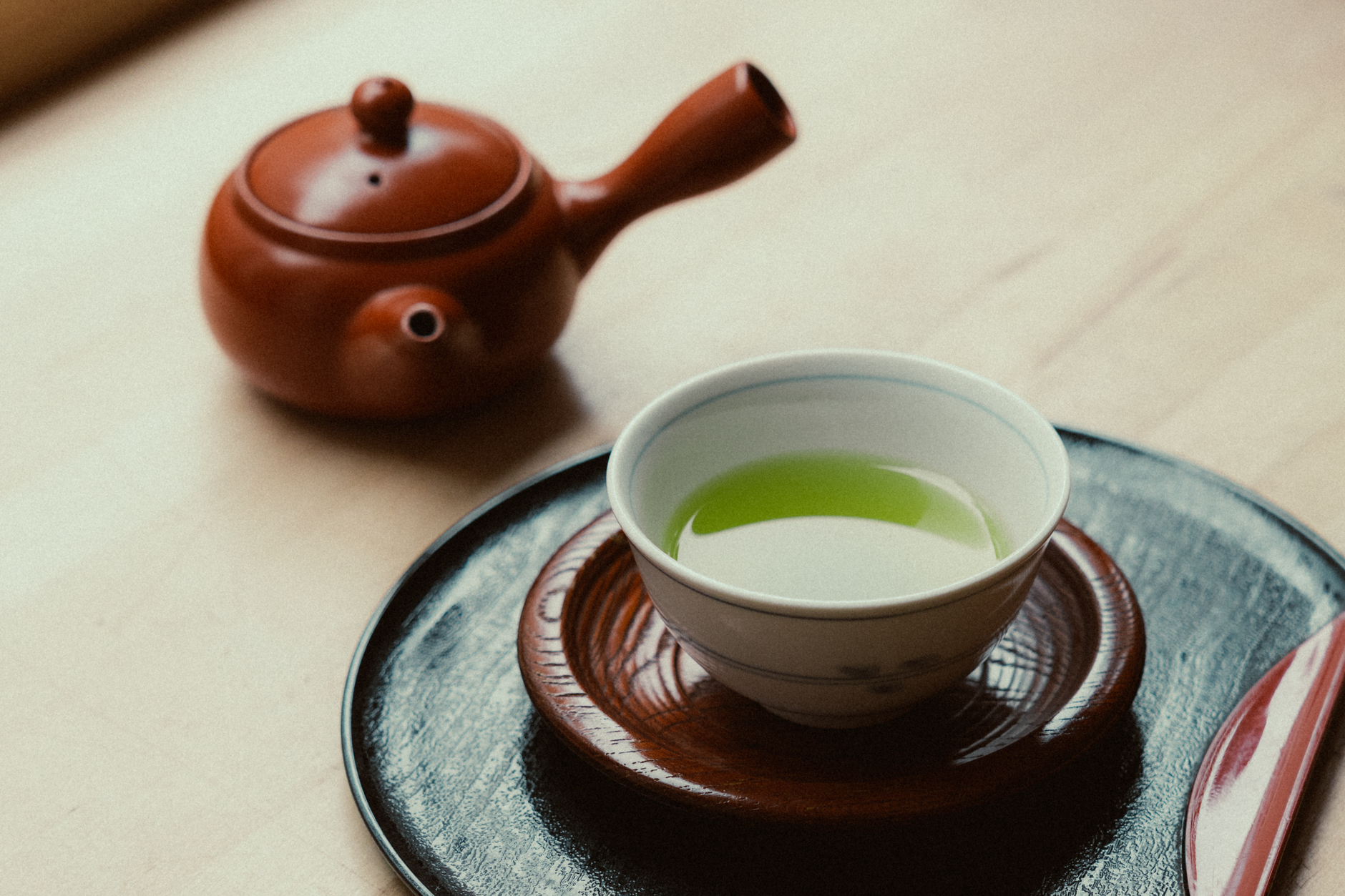 Steaming green sencha tea leaves unfurling in a white ceramic cup, releasing pale golden liquid against a minimalist background.