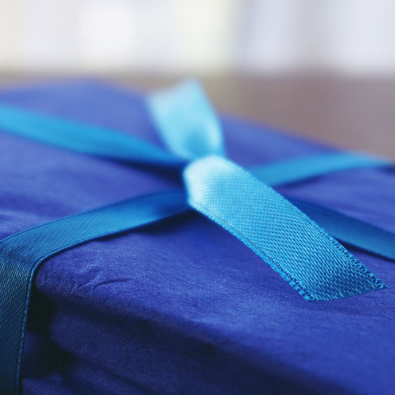 Traditional Japanese furoshiki cloth in indigo pattern wrapping a square box using the basic tsutsumi folding technique.