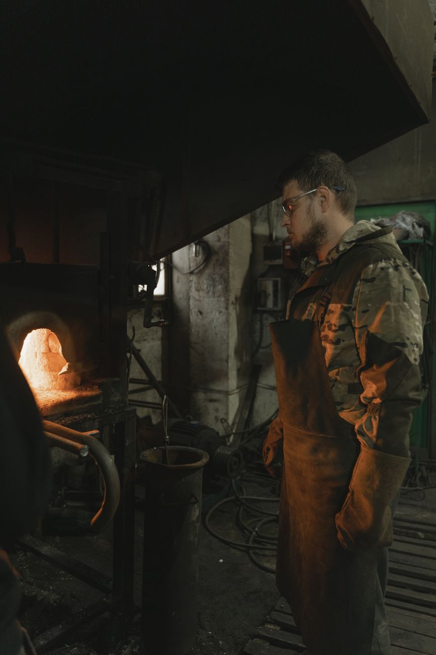 Artisan gathering molten Tsugaru Bidoro glass on a blowpipe from a furnace glowing with intense orange heat.