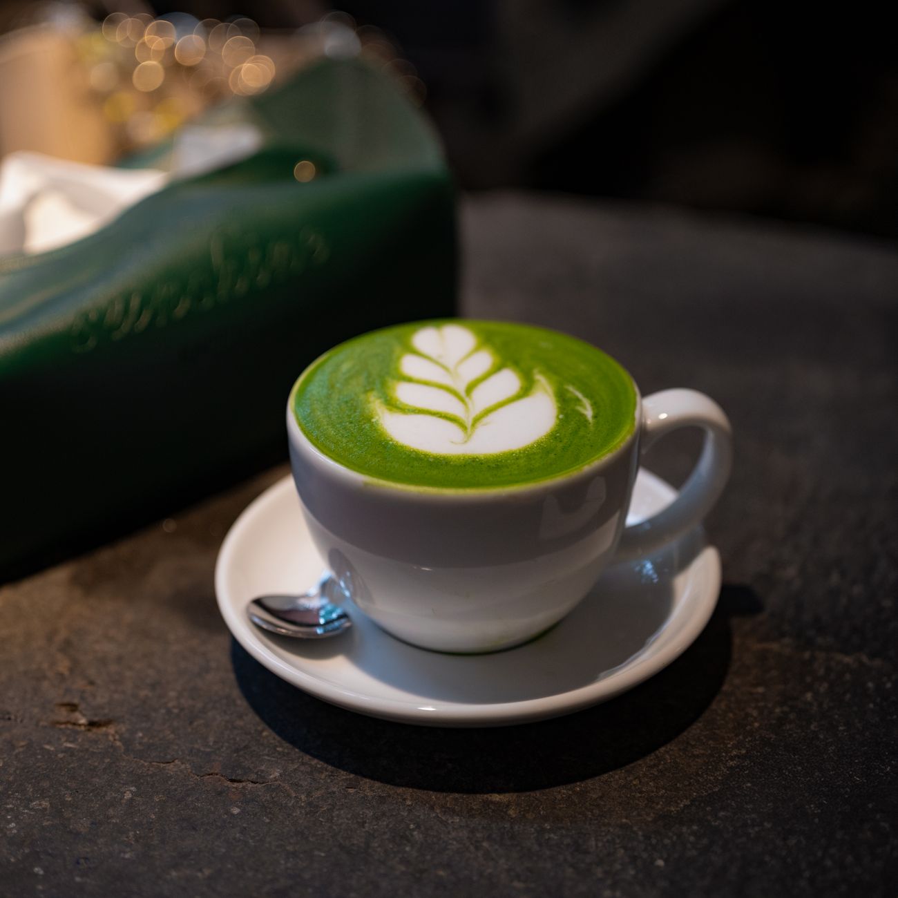 Vibrant green matcha powder in a ceramic bowl beside fresh sencha tea leaves on a bamboo mat.