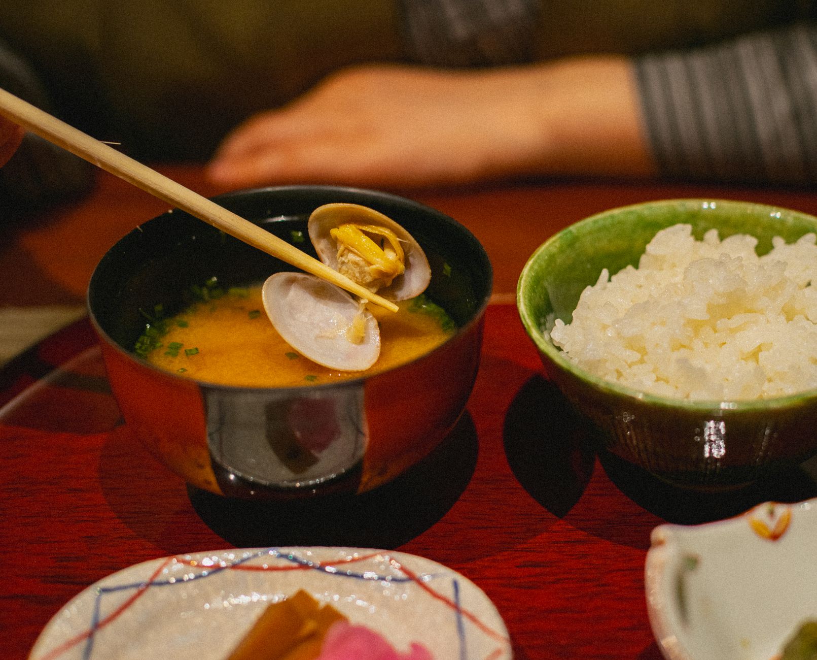 Hands straining kombu kelp and katsuobushi bonito flakes from steaming water in a traditional Japanese kitchen pot.