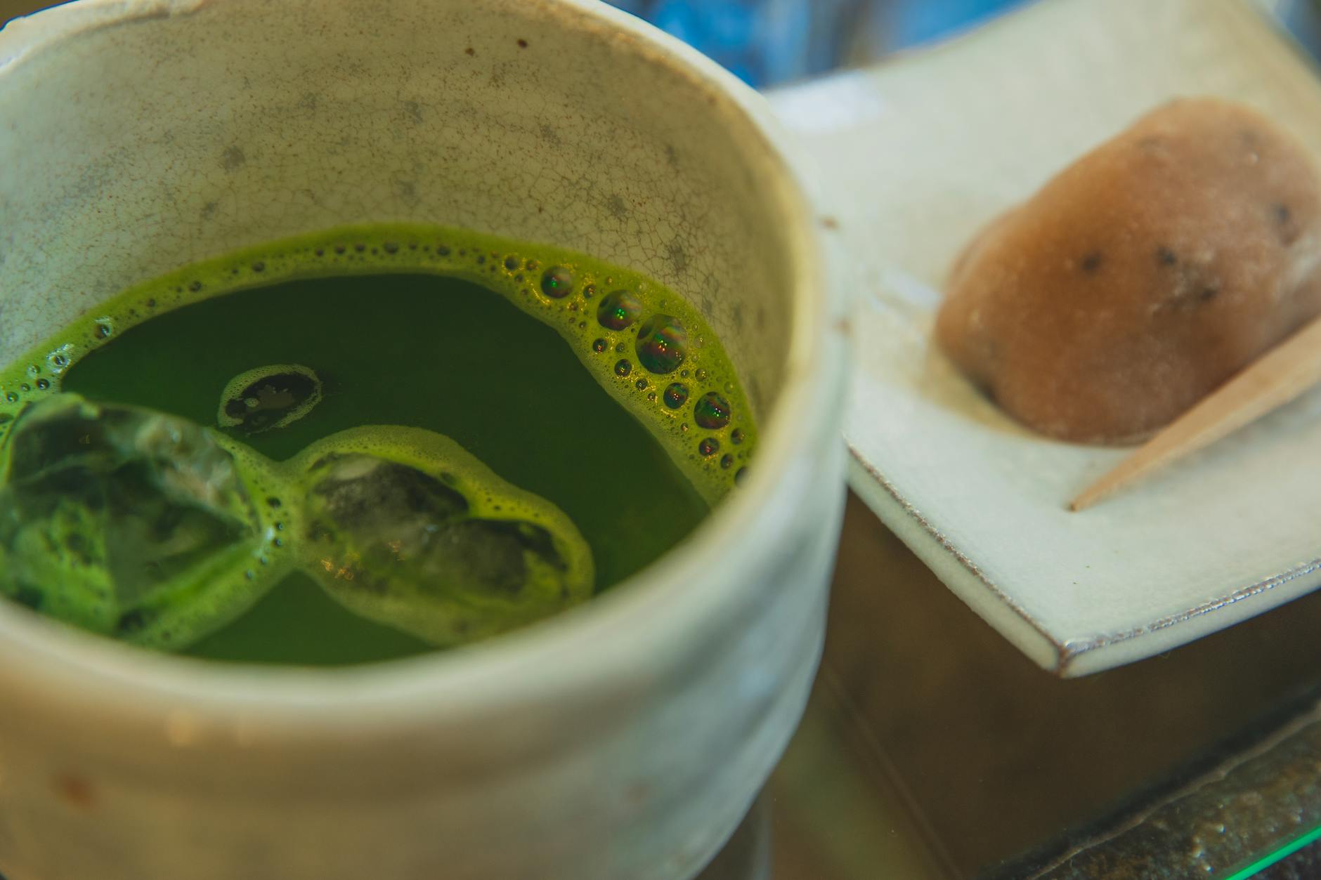 Side-by-side comparison showing bright green matcha powder in a bowl next to loose sencha tea leaves on a bamboo mat.