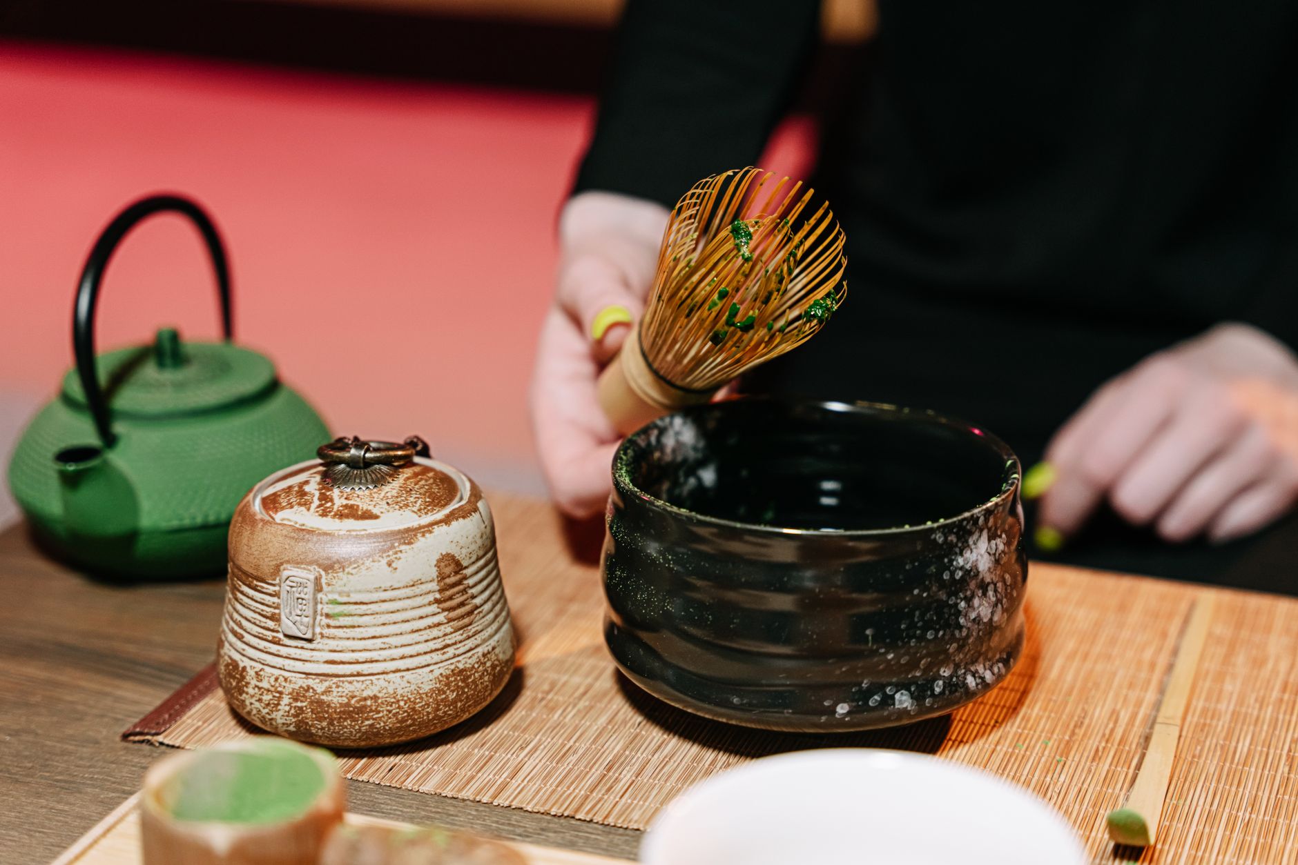 Matcha bowl positioned on tatami with seasonal wagashi sweets and a scroll depicting spring cherry blossoms in traditional tea room.