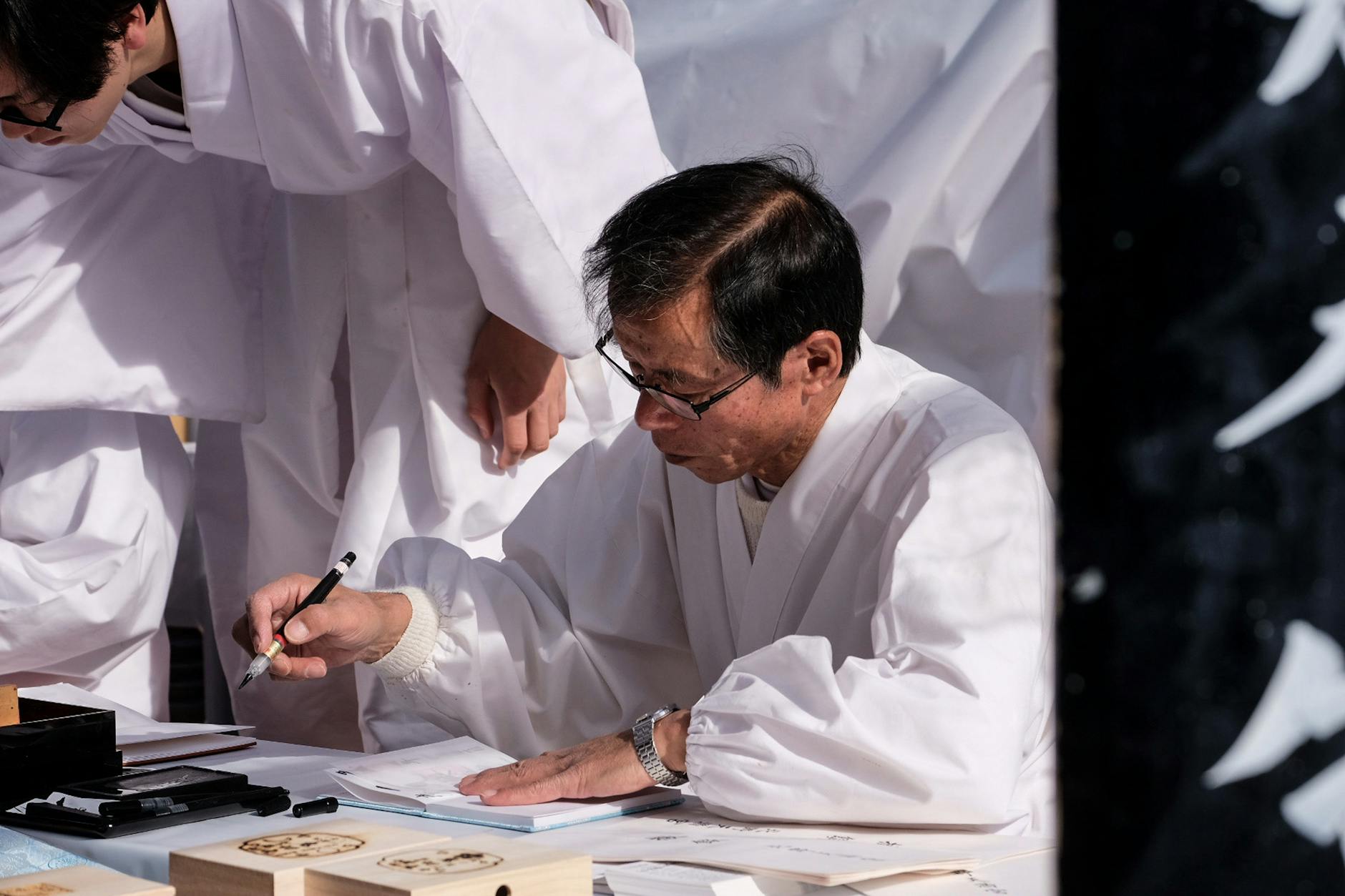 Black ink brush creating bold kanji strokes on white paper, showing fluid hand movement and varying line thickness in traditional shodo practice.