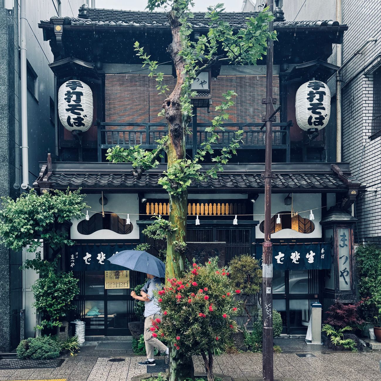 A person in traditional kimono bowing to enter through the low square entrance of a Japanese tea house.