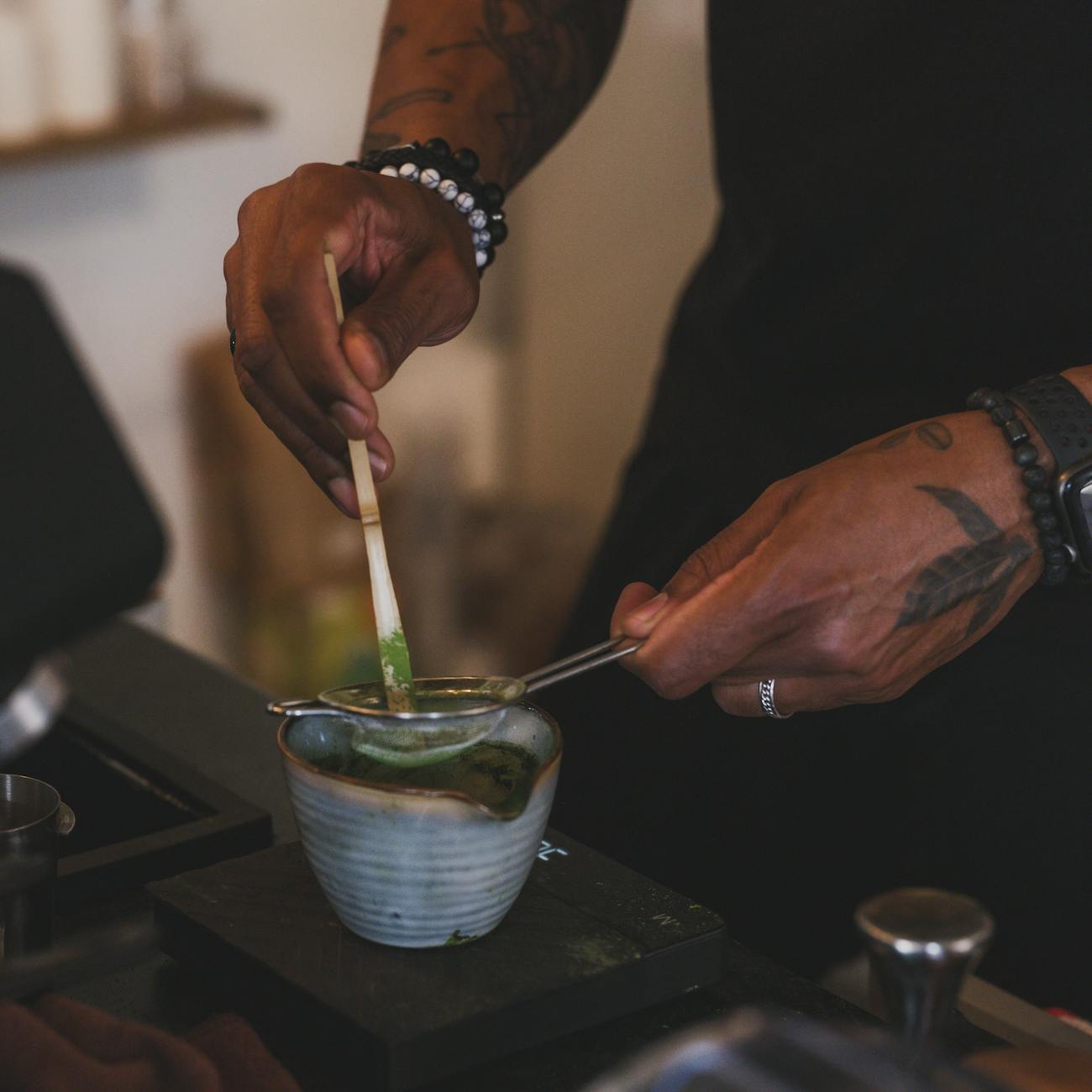 Vibrant green matcha powder in a ceramic bowl beside a bamboo whisk on a minimalist white surface.