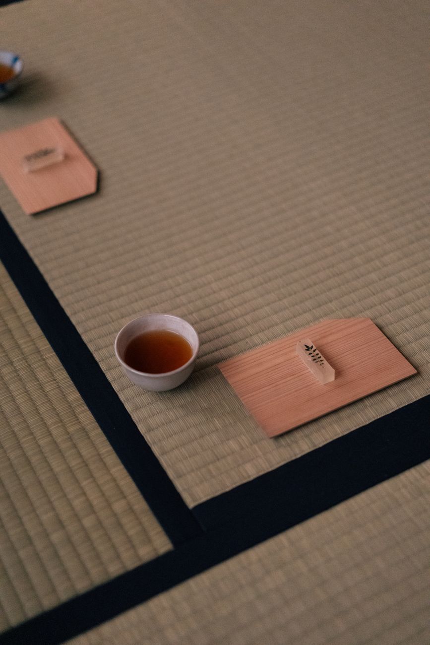 Traditional yunomi tea cup in earthy brown glaze resting on wooden table with green tea visible inside.