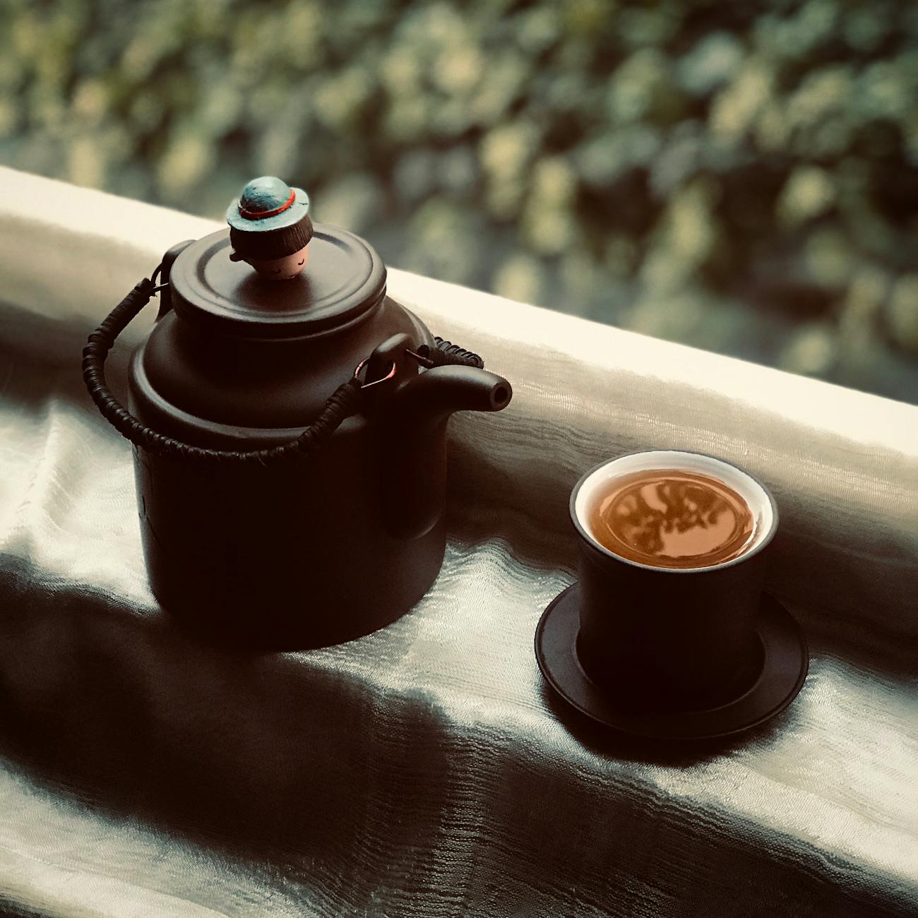 Traditional Japanese kyusu teapot with side handle pouring green tea into a small ceramic cup on wooden table.