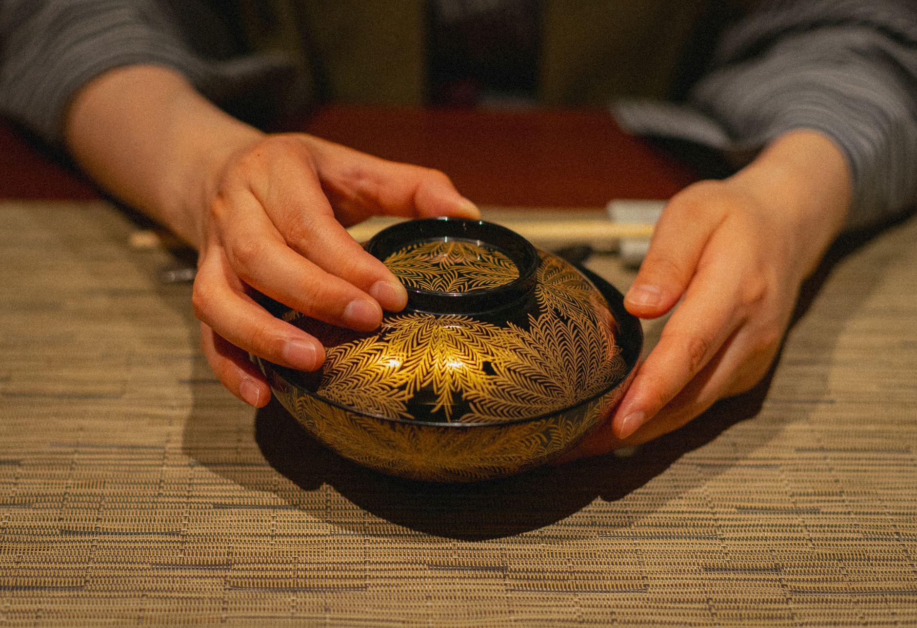 Hands applying gold lacquer to a cracked ceramic bowl on a wooden workspace with kintsugi tools and materials nearby.