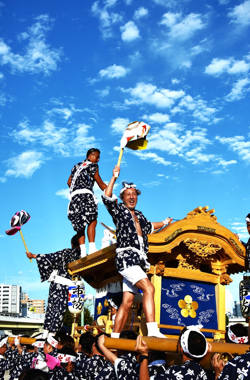 Colorful mikoshi portable shrine carried through crowded street during summer matsuri festival with paper lanterns overhead.