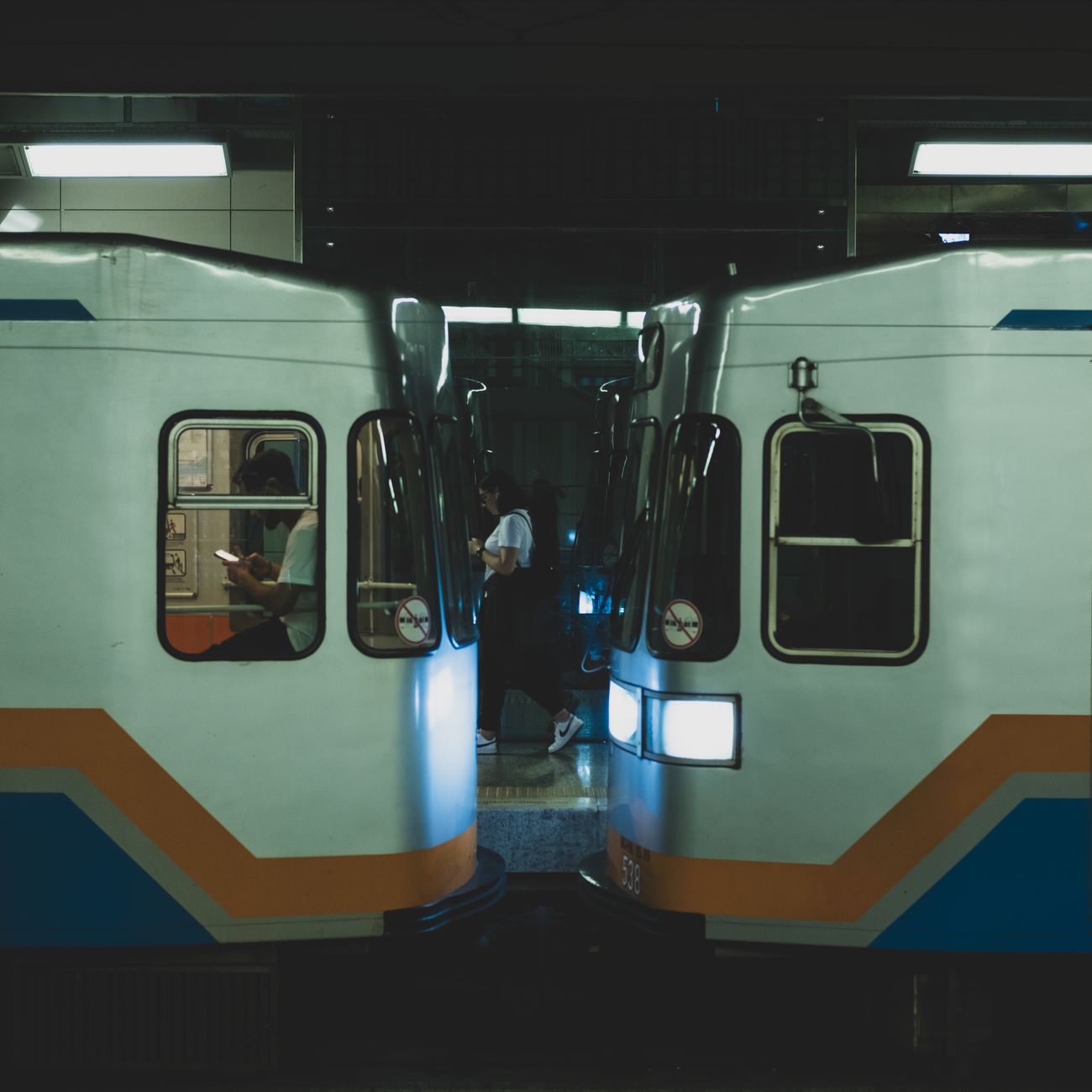 Japanese train conductor in uniform performing pointing and calling gesture toward departure board on railway platform.