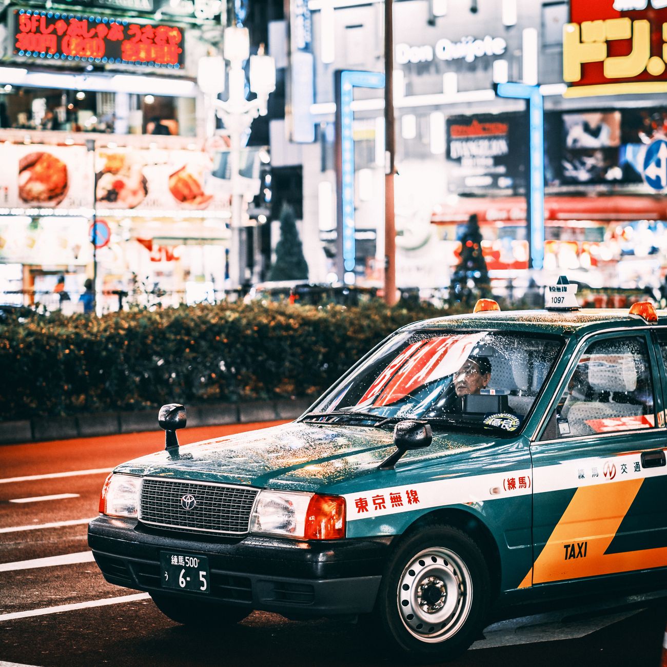 Busy Tokyo intersection with cars driving on the left side of the road beneath towering buildings and pedestrian crossings.