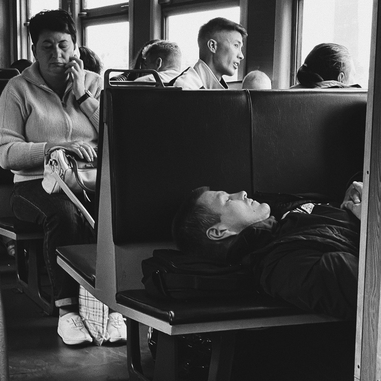 Japanese businessman in suit sleeping upright on train seat during morning commute, head tilted back with briefcase on lap.