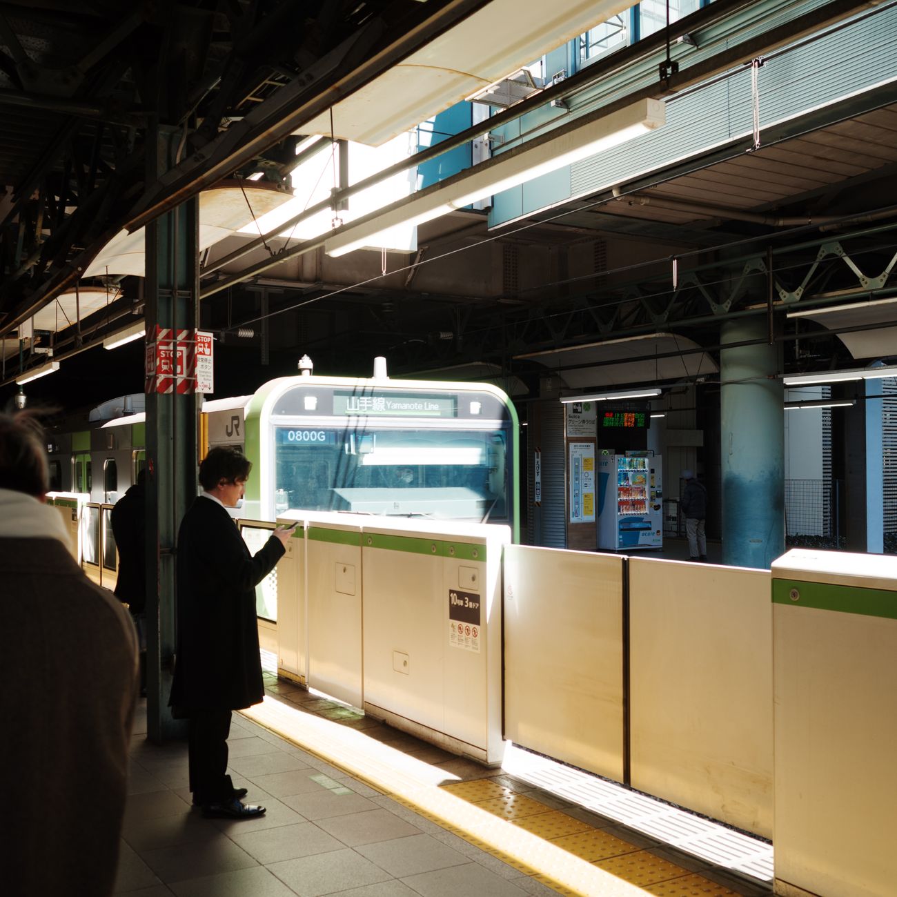 Japanese train conductor in navy uniform pointing at platform sign while wearing crisp white gloves at Tokyo station.