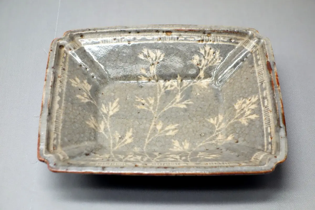 Traditional Mino ware pottery pieces displaying various glazing techniques including Shino, Oribe, and Kiseto on wooden shelves in Gifu Prefecture.