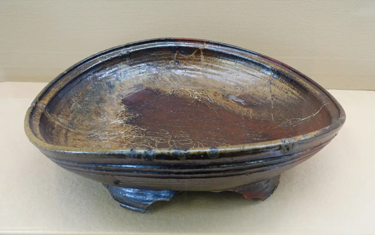 Traditional Bizen pottery vessels in earthy brown tones with natural ash glaze patterns from wood-firing, displayed on rustic wooden surface.