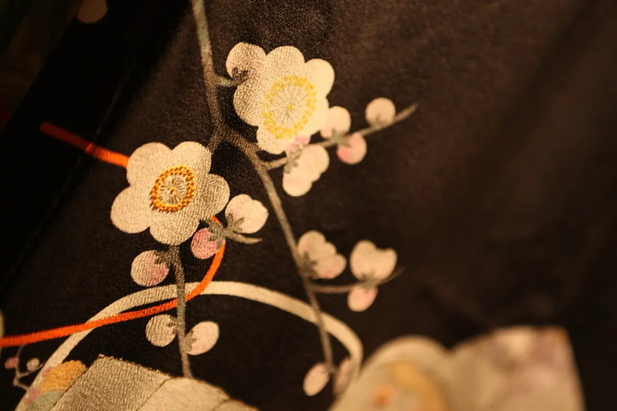 Artisan carefully hand-painting delicate plum blossoms onto silk kimono fabric using fine brush and vibrant natural dyes.