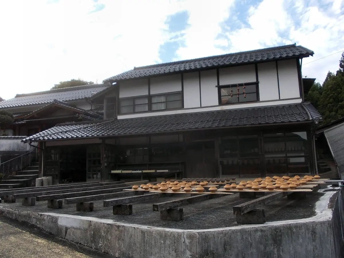 Traditional Onta pottery workshop nestled in forested mountains with wooden water-powered clay hammers and earthen kilns visible among trees.