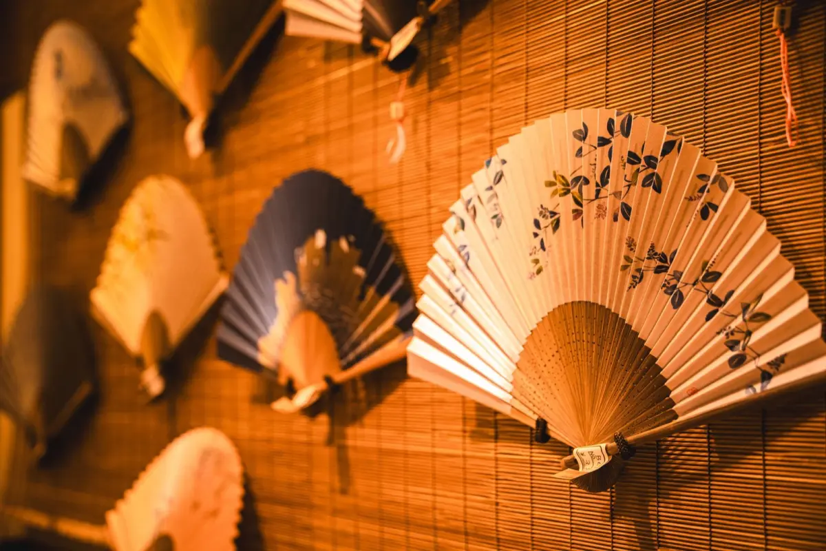 Artisan's hands applying colorful washi paper to bamboo frame of traditional Marugame uchiwa fan in workshop.