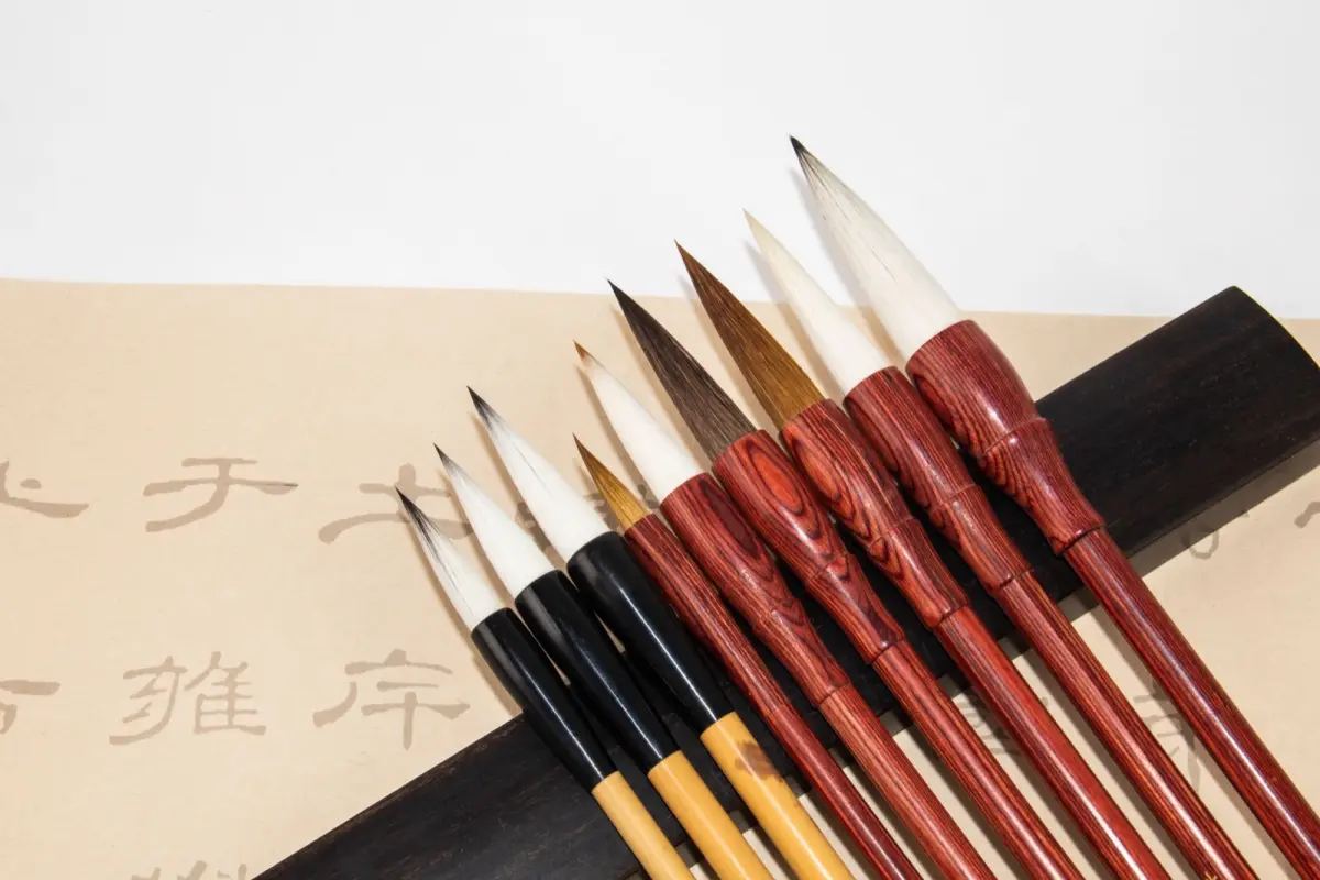 Artisan's hands carefully shaping a traditional Kumano makeup brush using natural animal hair in a sunlit Hiroshima workshop.