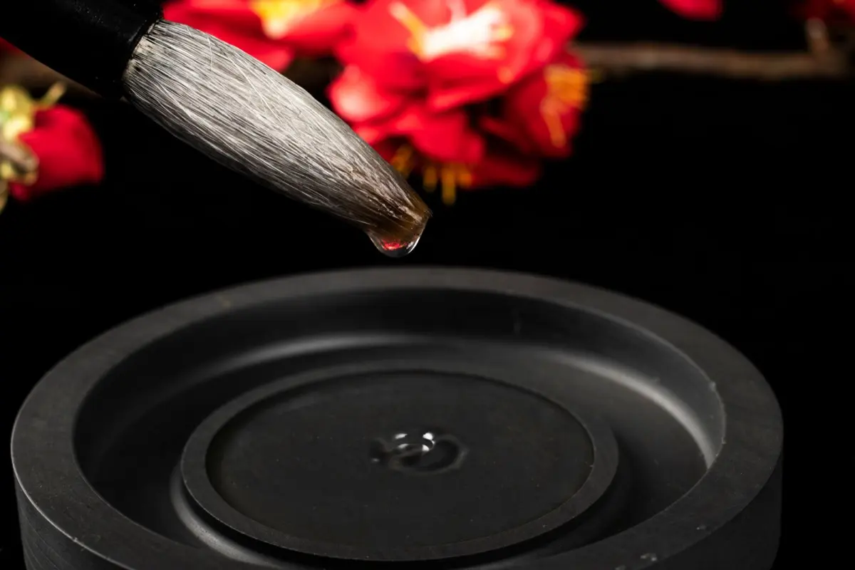 Artisan hand-carving intricate patterns into dark Ogatsu slate inkstone using traditional chisels in a sunlit workshop.