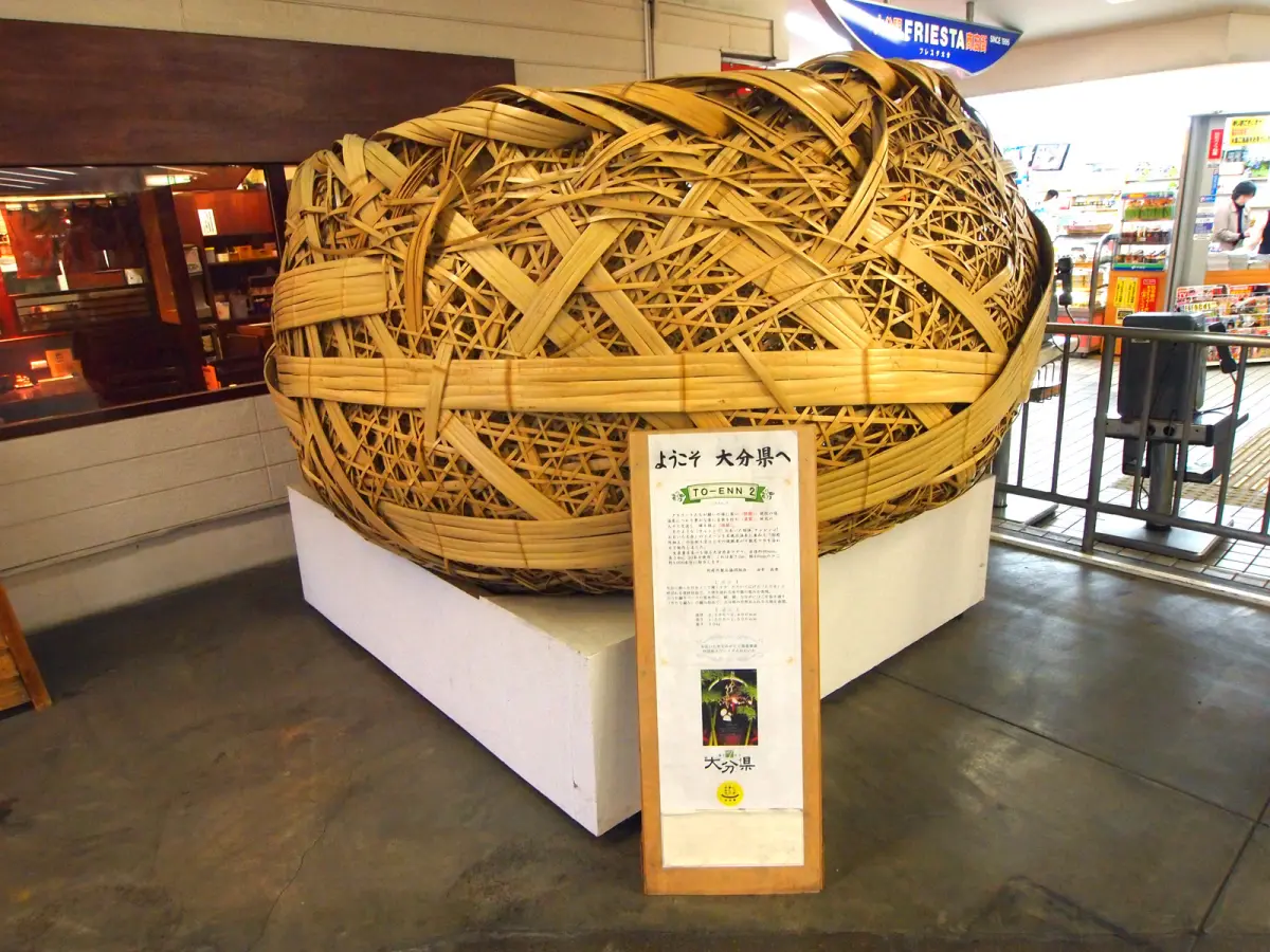 Artisan's hands weaving strips of golden bamboo into a delicate basket using traditional Beppu techniques in natural workshop light.