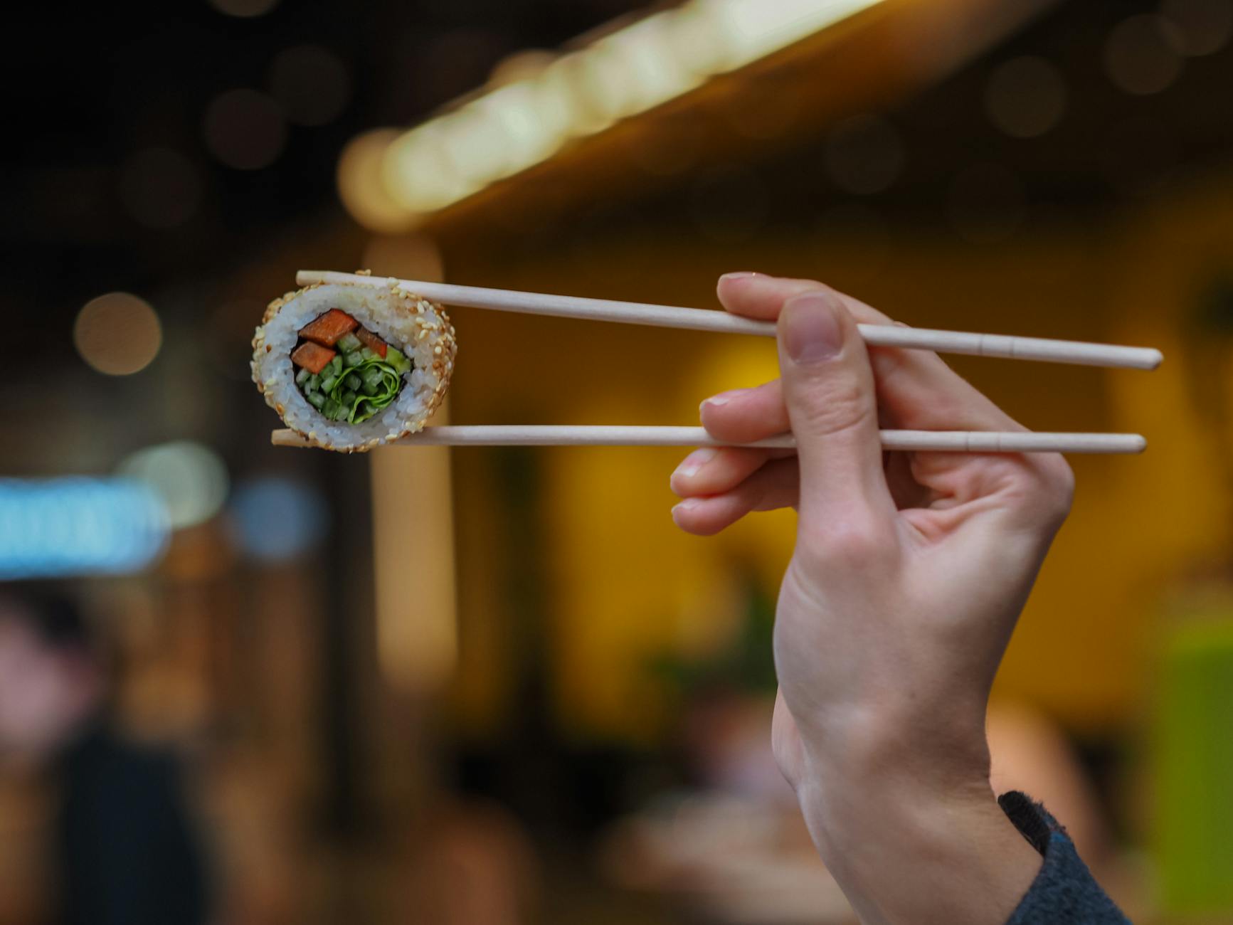 Hands demonstrating proper chopstick grip with thumb, index, and middle fingers positioned to hold two wooden chopsticks correctly.