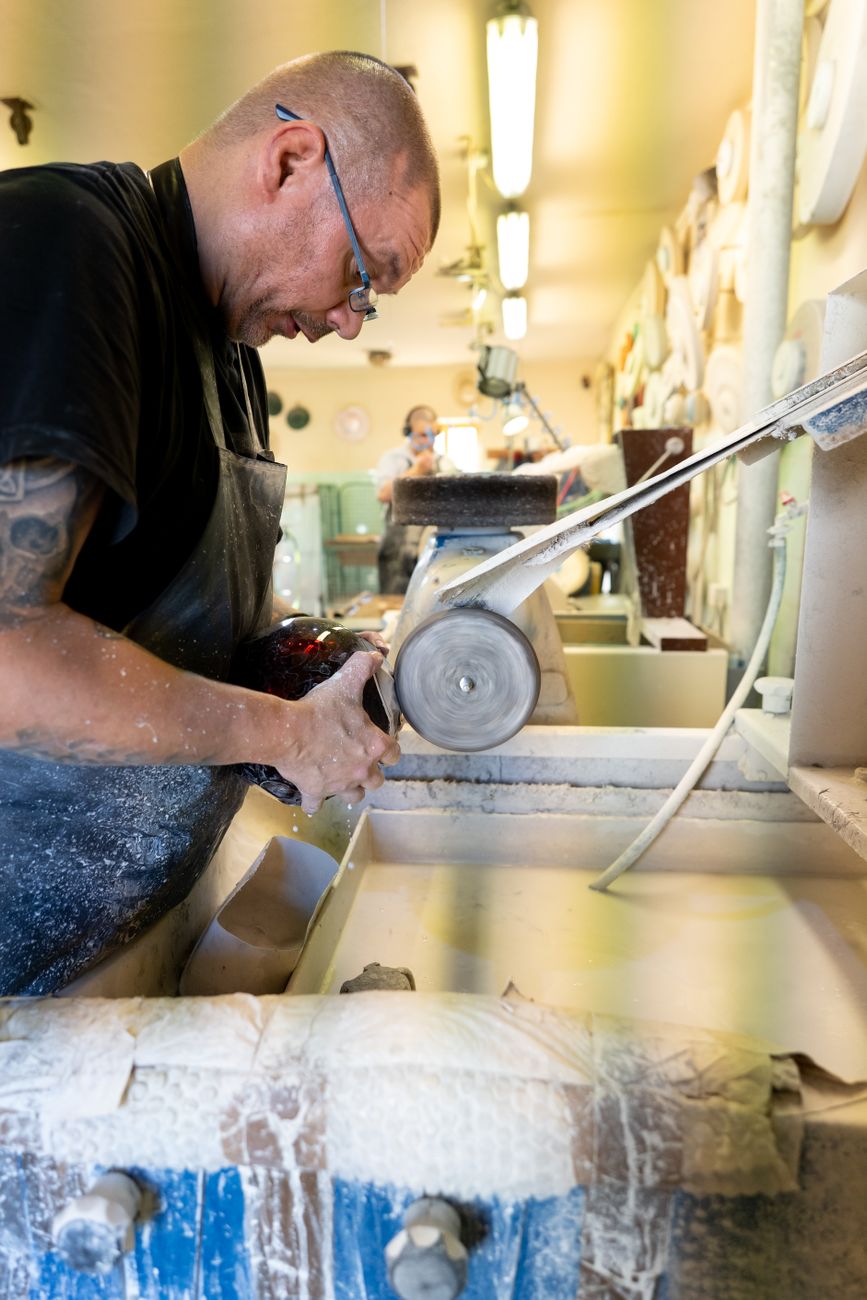 Artisan's hands guiding rotating crystal glass against a diamond-coated cutting wheel, creating precise geometric patterns in an Edo Kiriko workshop.
