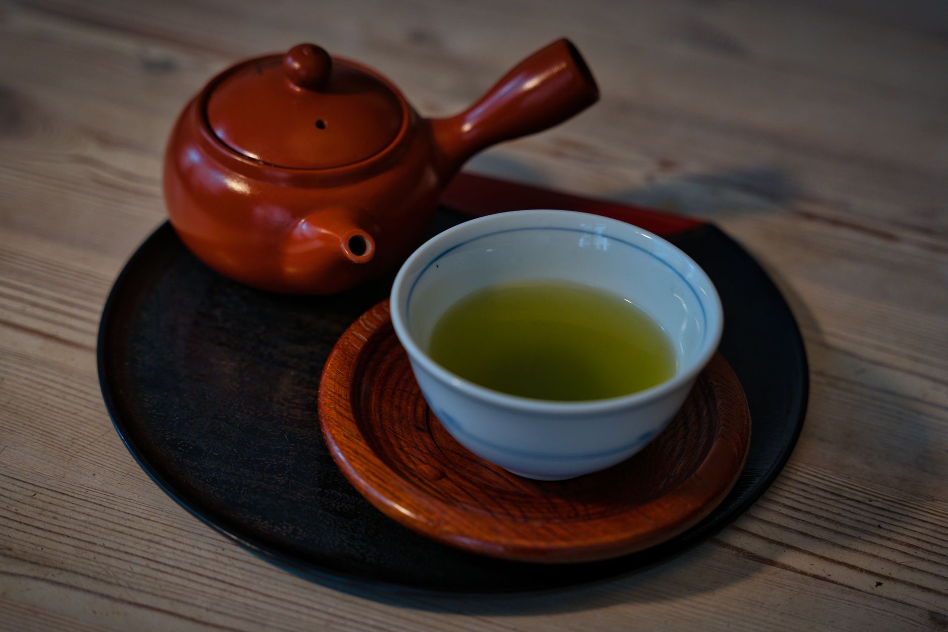 Loose green sencha tea leaves arranged beside a traditional Chinese gaiwan and Japanese kyusu teapot on wooden surface.