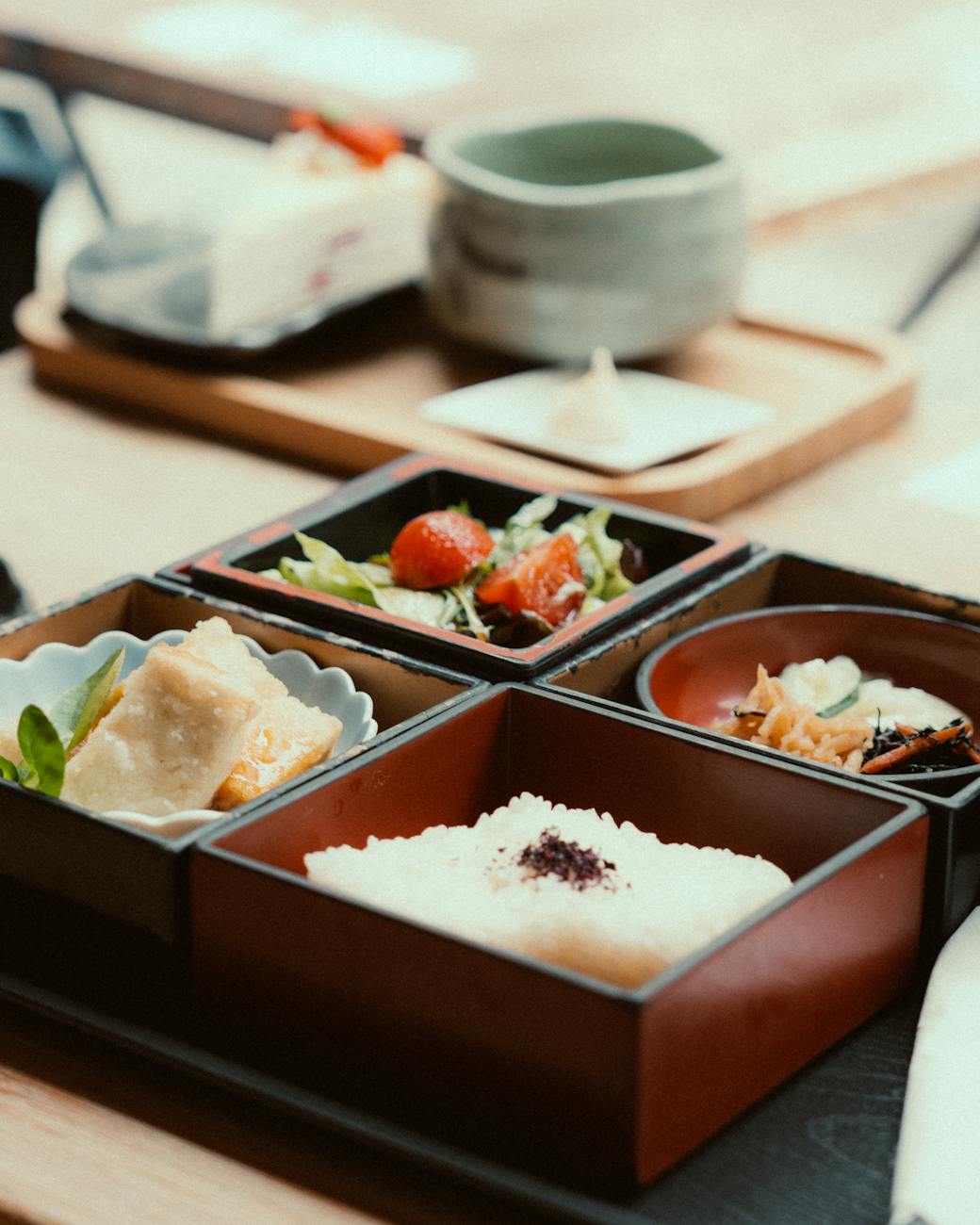 Traditional Japanese meal arrangement showing a bowl of miso soup, rice, grilled fish, pickled vegetables, and simmered vegetables on a wooden tray.