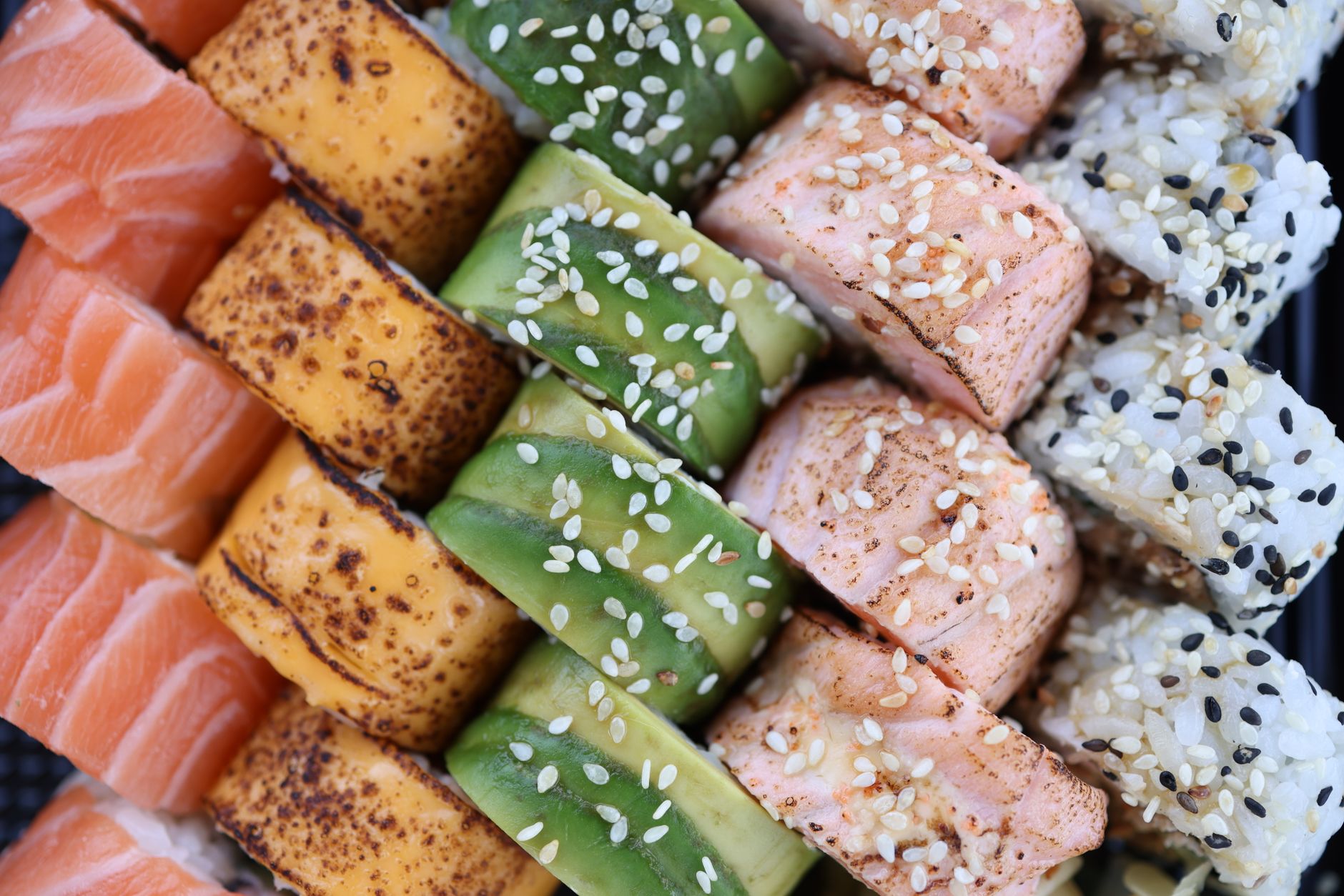 Traditional Japanese meal arranged on lacquerware featuring white rice, green vegetables, yellow pickles, red fish, and black sesame garnish.