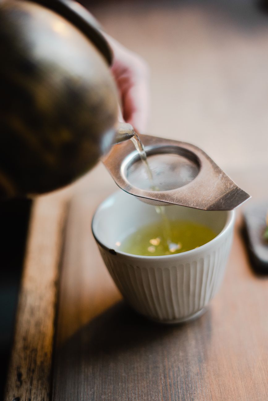 Side-by-side comparison showing Japanese green tea in a ceramic bowl beside Chinese oolong tea in a small porcelain cup.