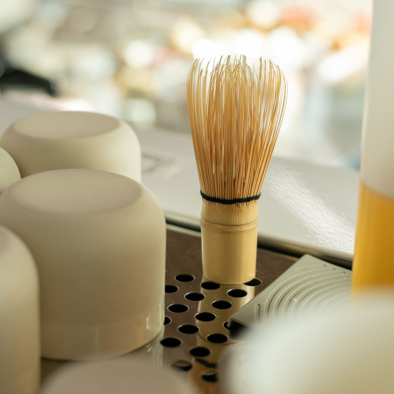 Traditional bamboo chasen with fine curved prongs next to a modern metal kitchen whisk on a tea preparation surface.