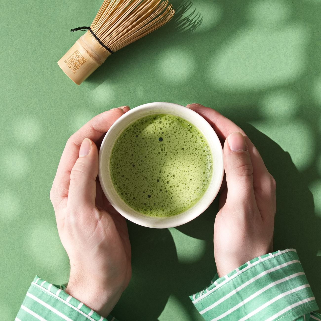 Bamboo chasen whisking vibrant green matcha powder in a ceramic bowl, creating smooth foam with traditional W-shaped hand motions.