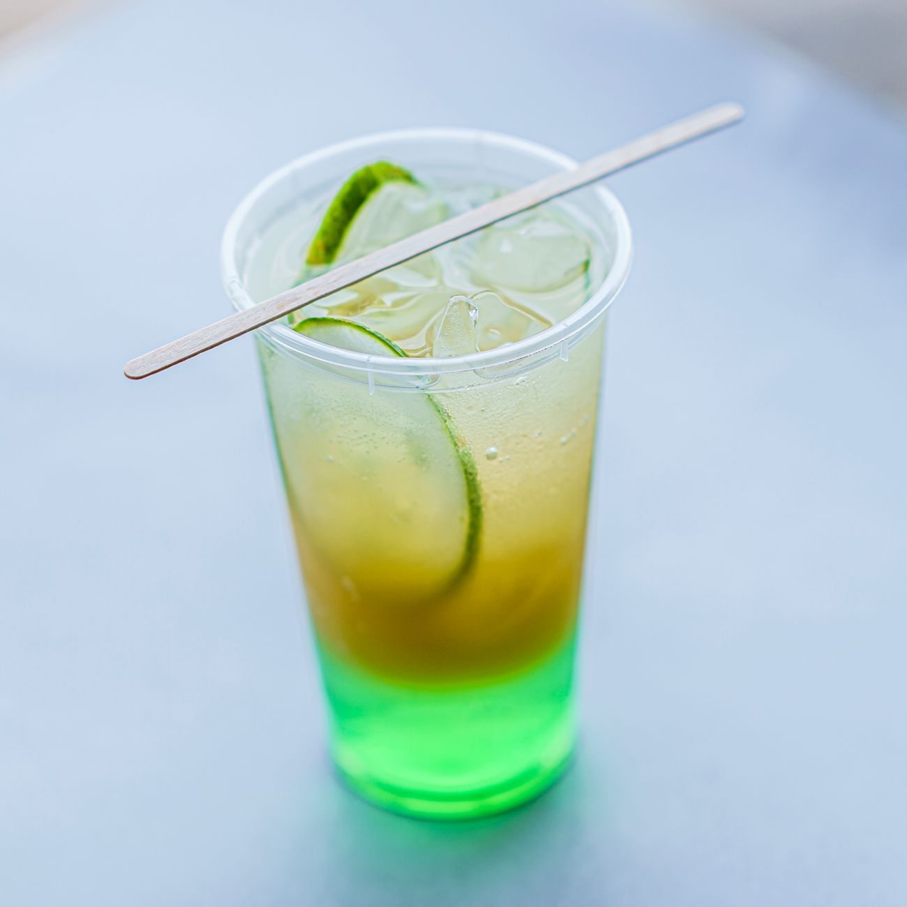 Glass pitcher filled with pale green cold brew tea beside fresh sencha leaves on a wooden table