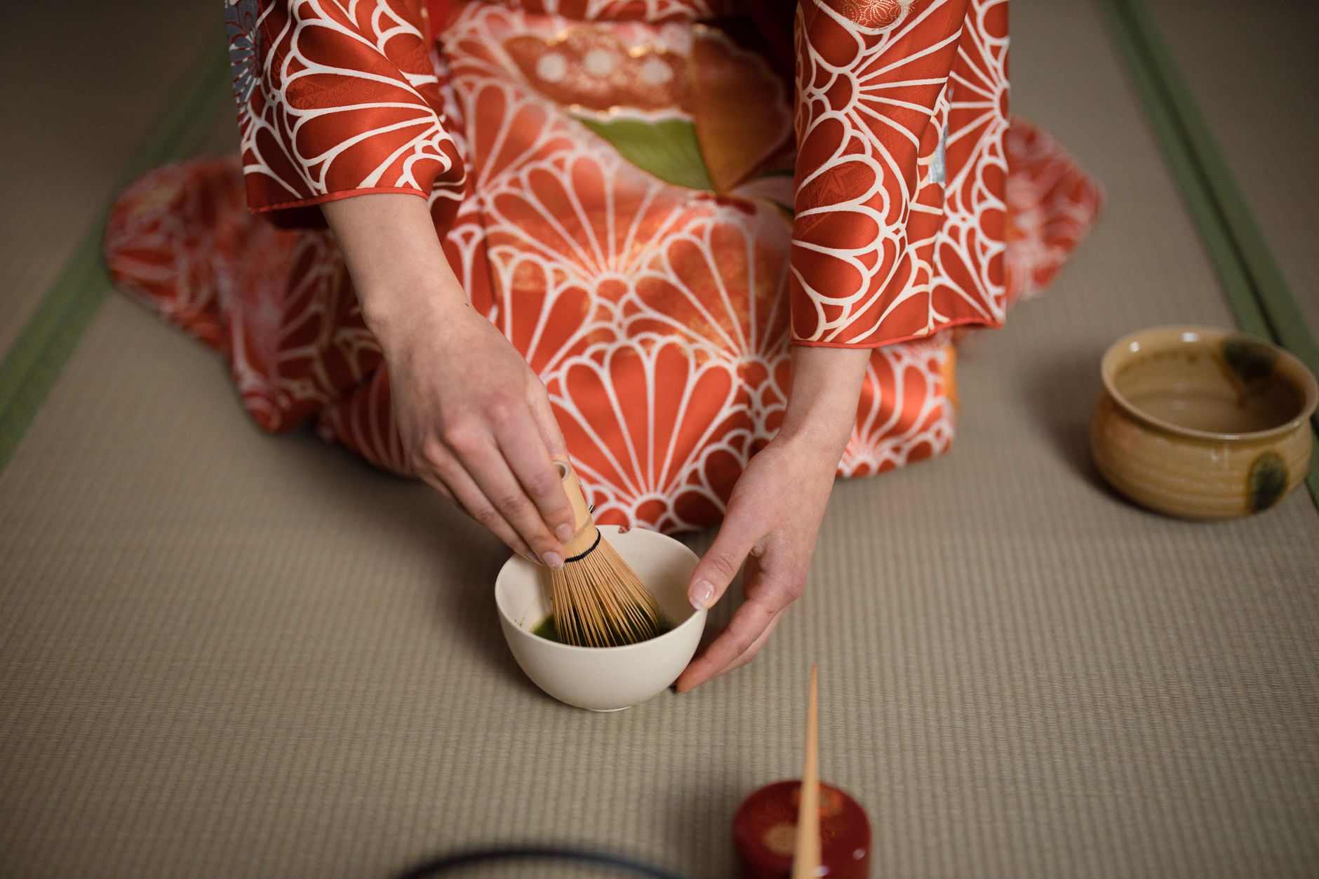 Bamboo chasen whisk creating foam in a ceramic bowl of vibrant green matcha tea with traditional preparation technique