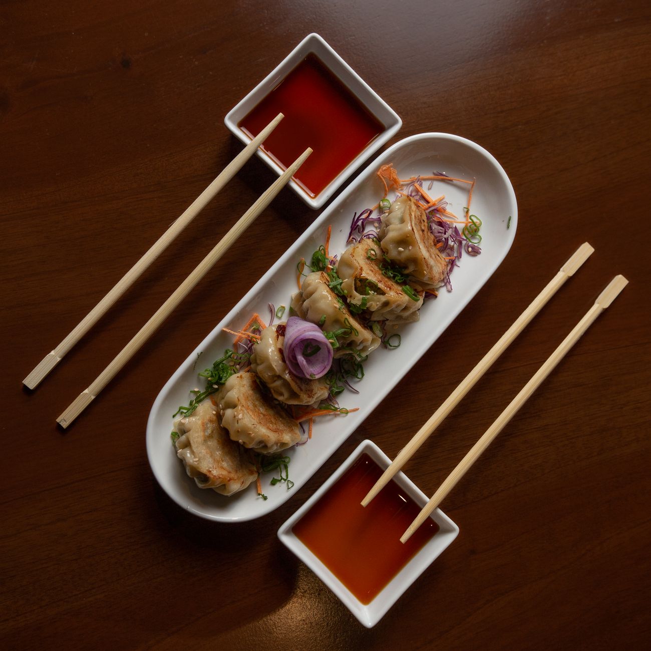Nigiri sushi piece being gently dipped fish-side down into a small ceramic dish of dark soy sauce.