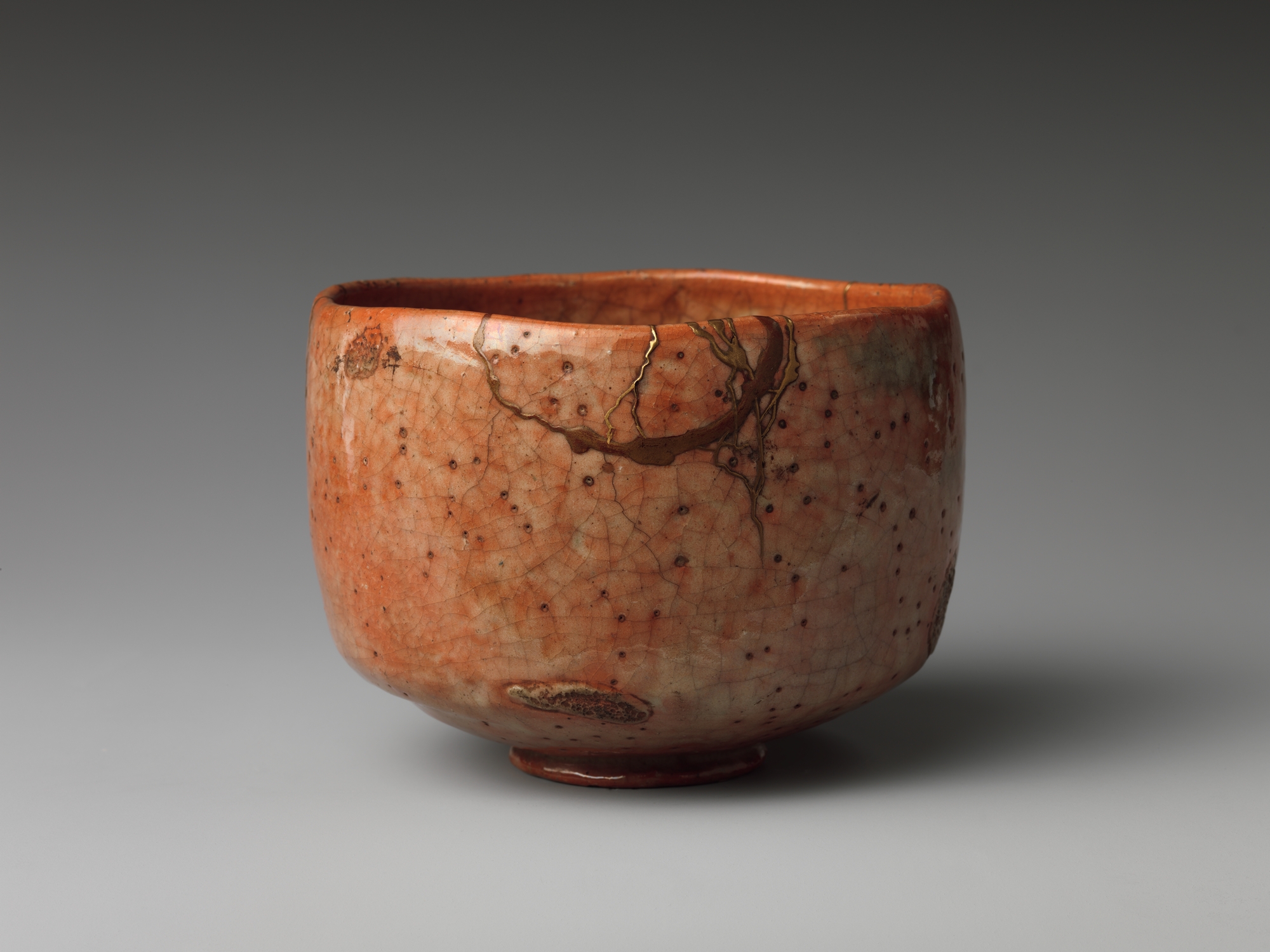 18th-century orange-red Raku tea bowl with a visible gold kintsugi repair line running through a crack