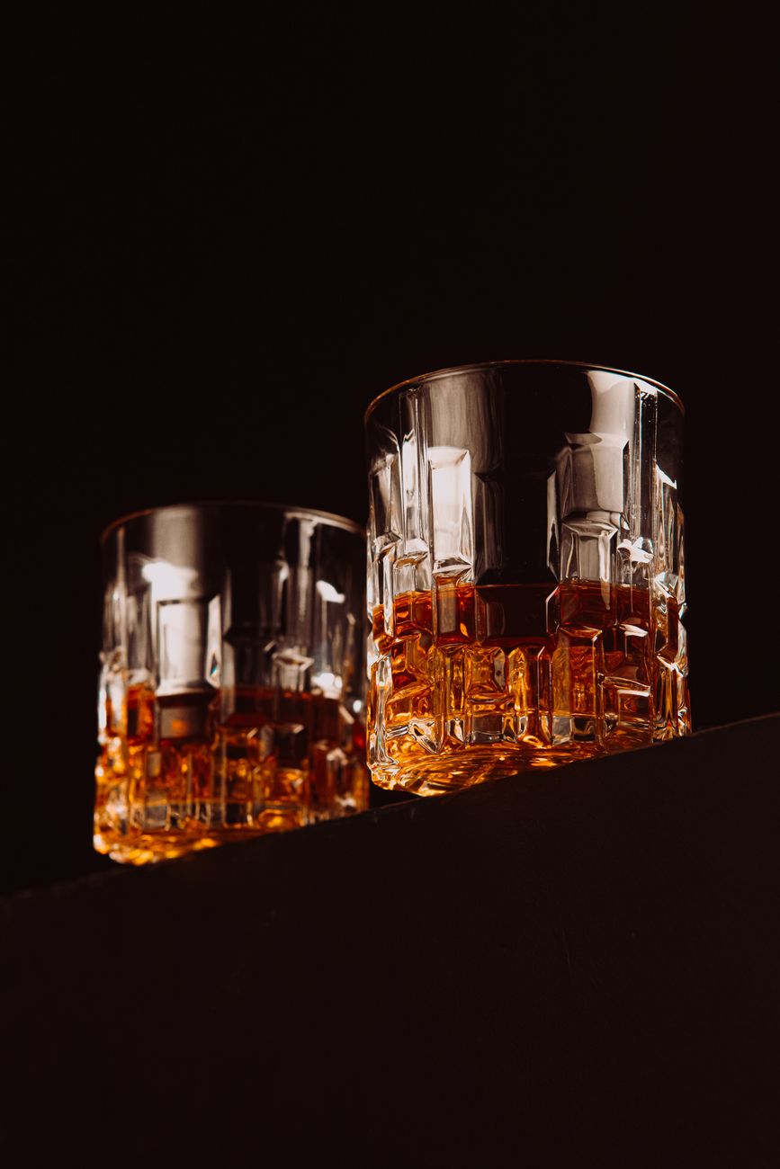 Pair of cut-crystal rock glasses with amber whiskey, geometric facets catching warm light against a dark background