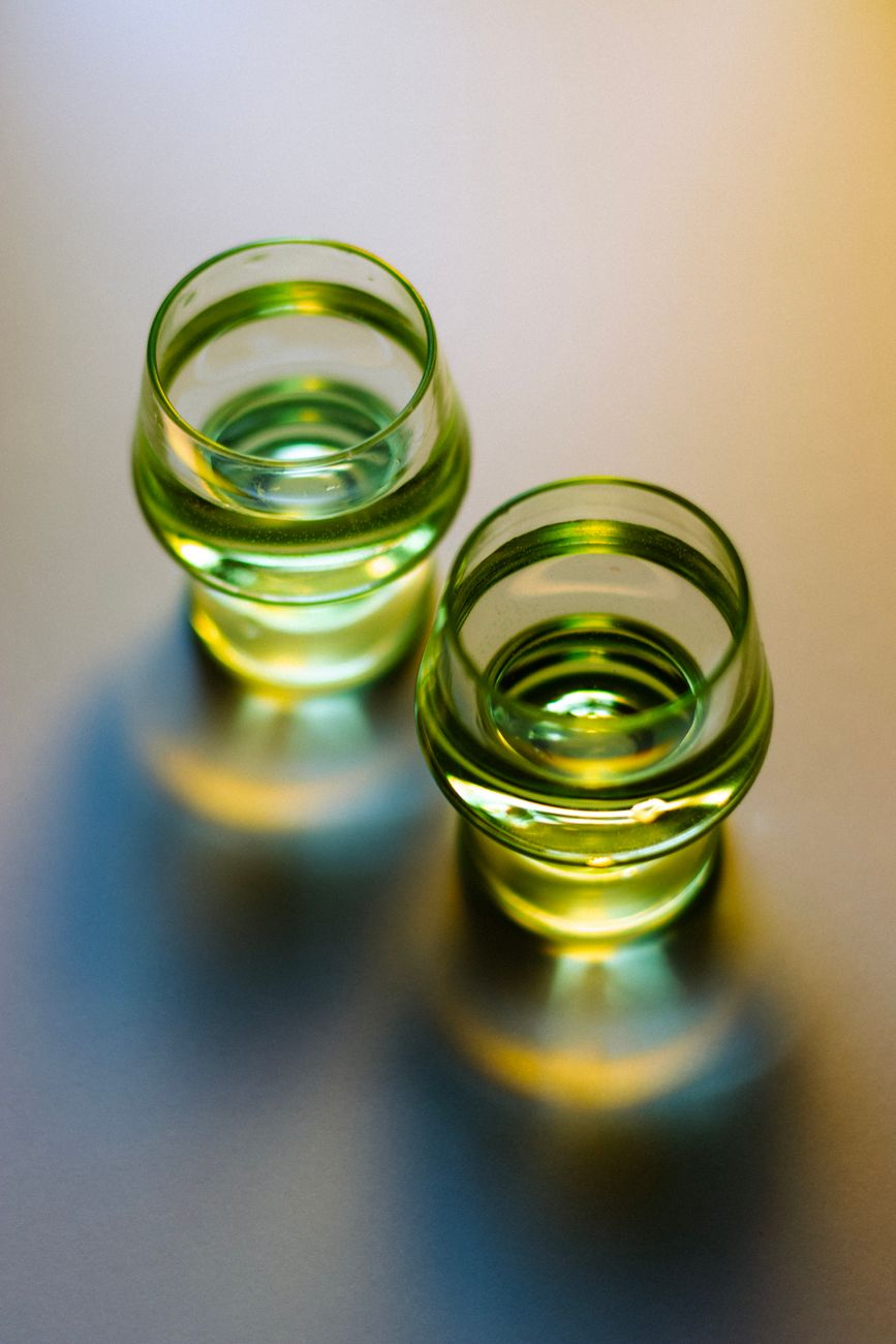 Two small green glass cups filled with liquid, lit from above showing color pooling at the base of each cup