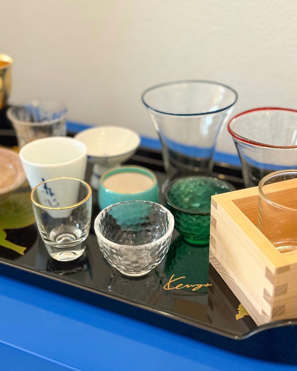 Tray of assorted mismatched Japanese sake cups in glass and porcelain, different colors and shapes, displayed together
